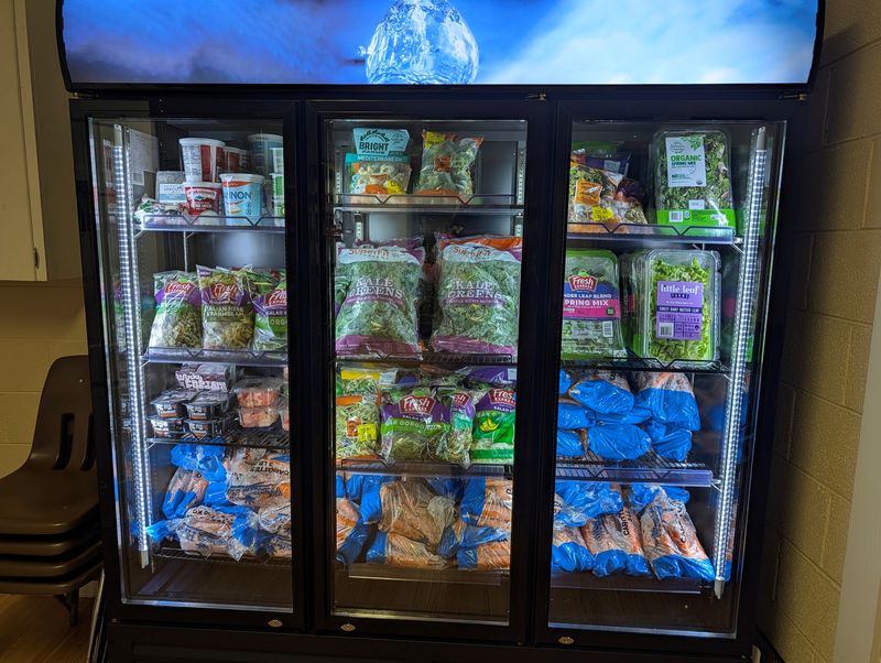 Glass-door cooler at CRS stocked with fresh kale, salad greens, spring mix, yogurt and bagged carrots